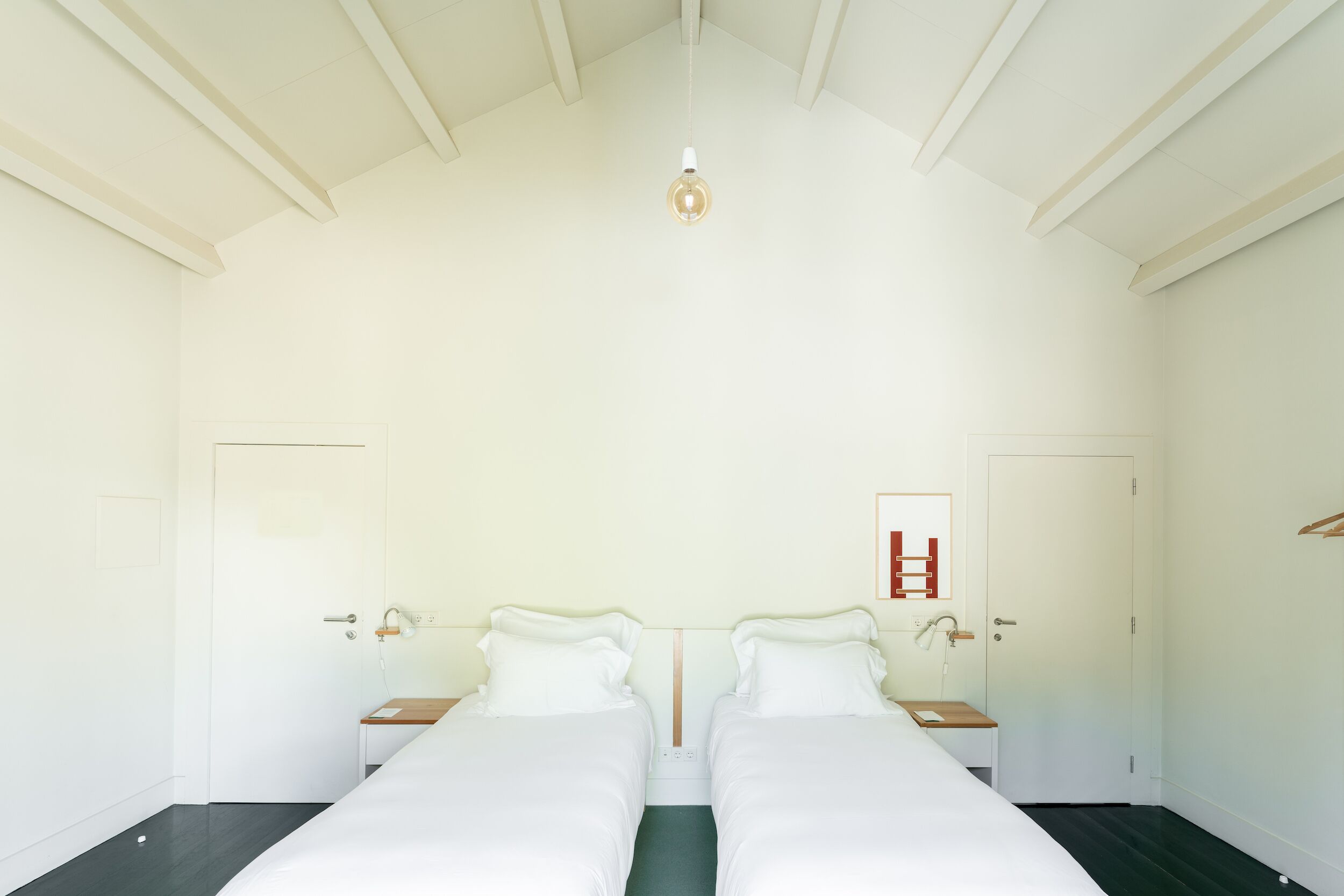 Quarto com duas camas, luminária pendente e porta com placa vermelha.