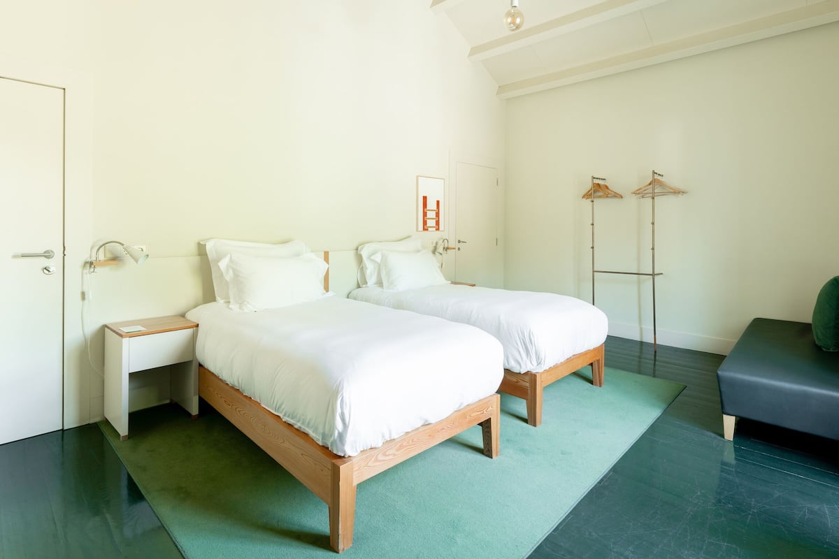 A bedroom with two wooden beds, a bedside table, a hanging light, and a coat rack.