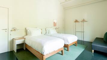 A bedroom with two wooden beds, a bedside table, a hanging light, and a coat rack.