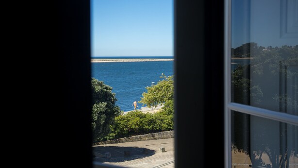 Een uitzicht op een kustgebied met een helderblauwe lucht, een zandstrand en iemand die langs de kust wandelt.