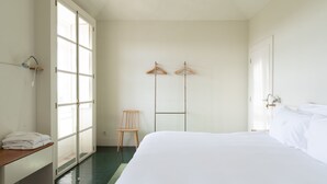 Een minimalistisch hotelkamer met een groot bed, een houten stoel en een garderobe met spiegel.