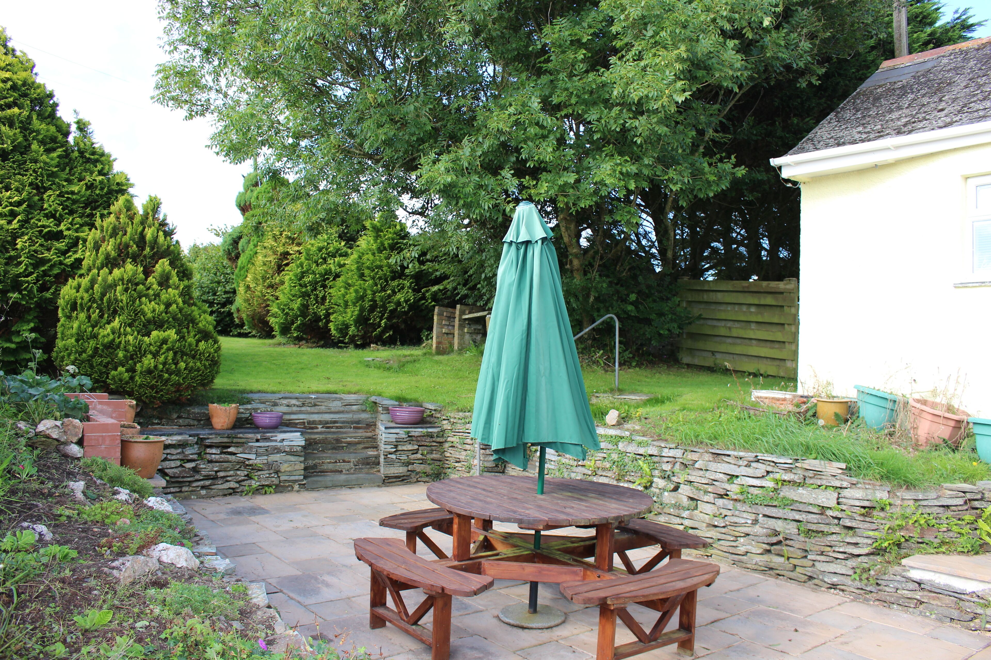 A wooden picnic table with benches and a green umbrella in a garden setting.