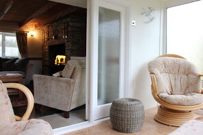 Un salon chaleureux avec une cheminée en pierre, un pouf en osier et un fauteuil confortable.