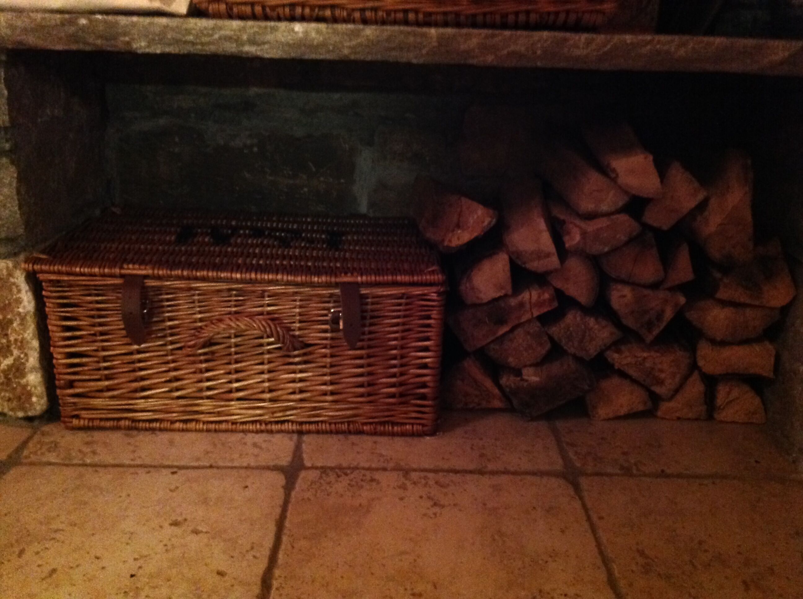 A wicker basket and a stack of firewood in a stone-walled room.