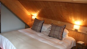 Ein Schlafzimmer mit Holzbalkendecke, einem großen Bett mit weißer Bettwäsche, zwei Nachttischlampen und einem Nachttisch mit einem Buch und einem herzförmigen Gegenstand.