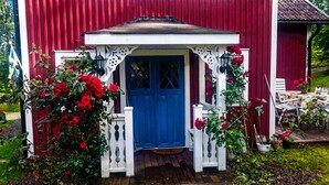 A red barn with a blue door, white porch, and red roses. - Nice old style cottage close to the Baltic Sea (Gryt, Valdemarsvik)