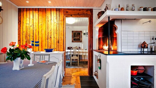 A kitchen with a wooden wall, a dining area, and a built-in stove. - Nice old style cottage close to the Baltic Sea (Gryt, Valdemarsvik)
