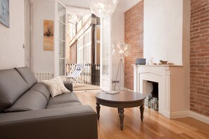 A living room with a grey sofa, a round wooden table, a white fireplace, and a brick wall. - BEST CENTRAL CITY LOCATION MODERN 3 BED APT PRIVATE TERRACE PERFECT FOR FAMILIES (Barcelona)