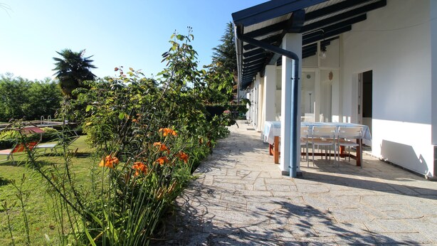 A covered outdoor seating area with tables and chairs, a stone pathway, and a garden with orange flowers.