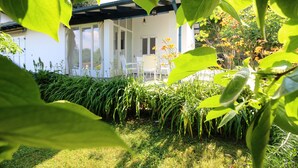 A white house with a covered patio, surrounded by lush greenery and plants.