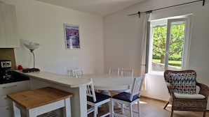 A kitchen with a dining table, chairs, a wicker chair, a small table, and a shelf unit.
