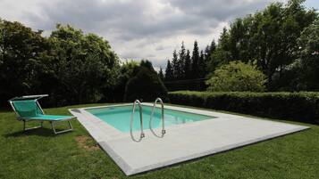 A rectangular swimming pool with two ladders, surrounded by a grassy area and trees.