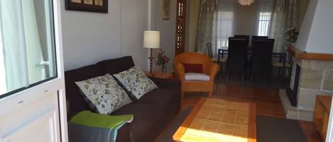 A living room with a sofa, a chair, a table, and a dining area with chairs and a table.