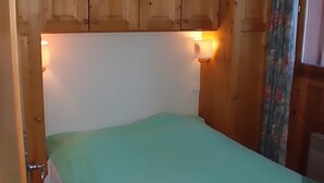 Une chambre avec une couvre-lit verte, des armoires en bois au-dessus du lit et deux lampes fixées au mur.