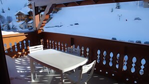 Un balcon avec une table et des chaises, donnant sur un paysage montagneux enneigé.