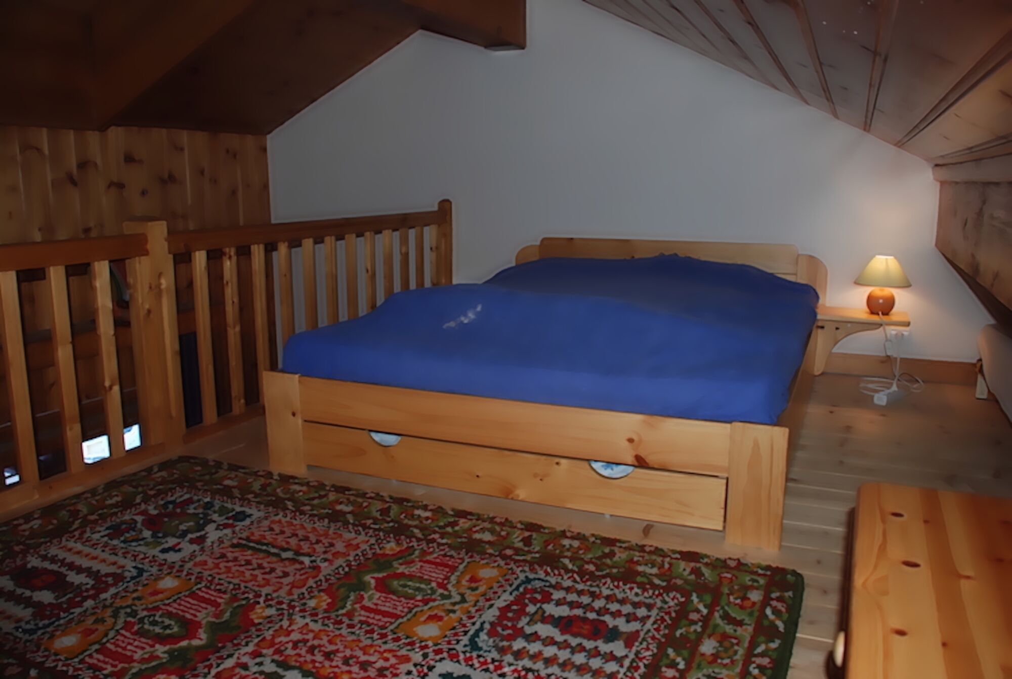 A wooden bed with a blue mattress in a room with wooden walls and a sloped ceiling.