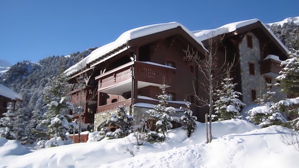 Un chalet à plusieurs étages, doté de balcons, entouré d’arbres et de montagnes couverts de neige.