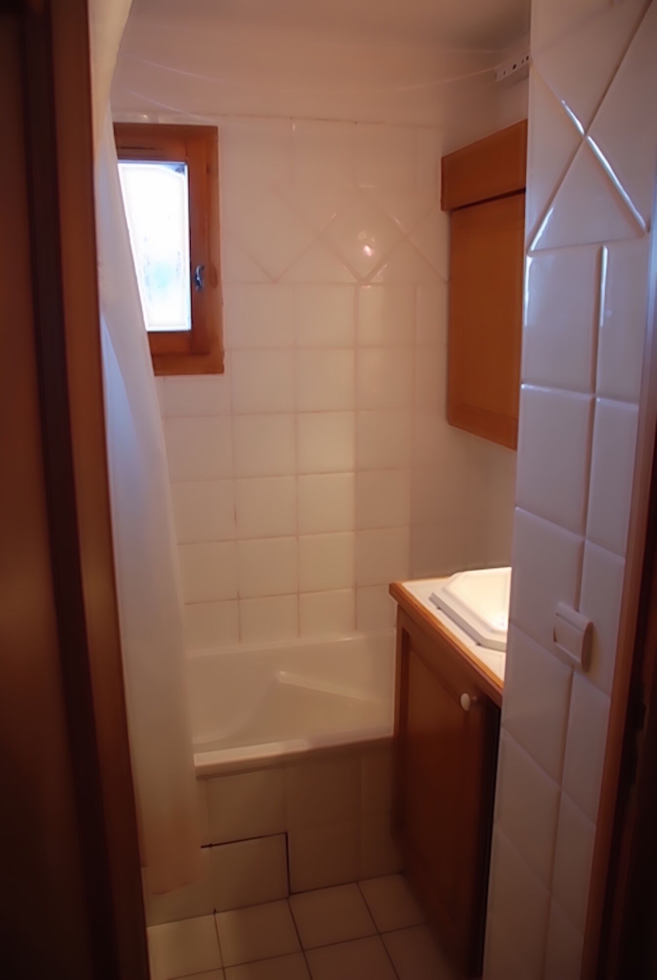 A small bathroom with a shower, a window, and a wooden cabinet.