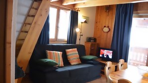 Un salon chaleureux avec un canapé foncé, une table en bois et un téléviseur.