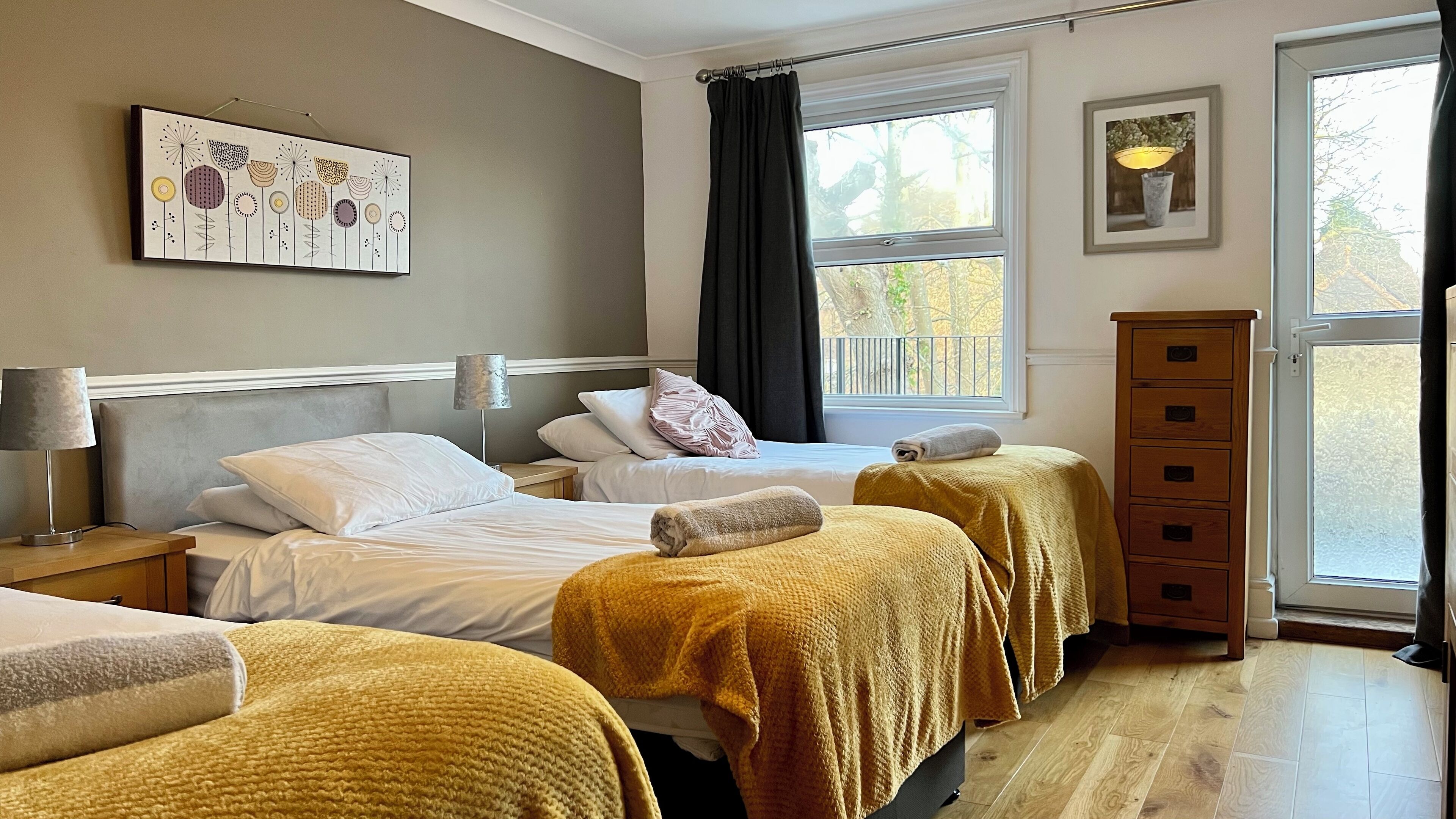 A hotel room with two beds, a nightstand with a lamp, a dresser, and a window with a view of trees.