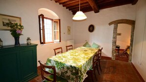 A dining area with a table set for four, a green cabinet, and a window with curtains. - Ancient stone house in the heart of the Chianti Classico (Panzano in Chianti)