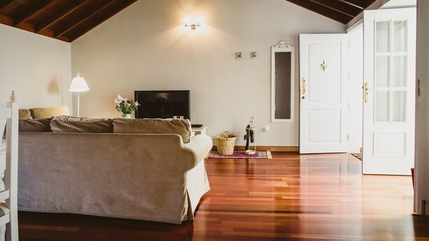 Ein geräumiges Zimmer mit Holzboden, einer Couch, einem Fernseher und einer Tür zu einem anderen Raum.