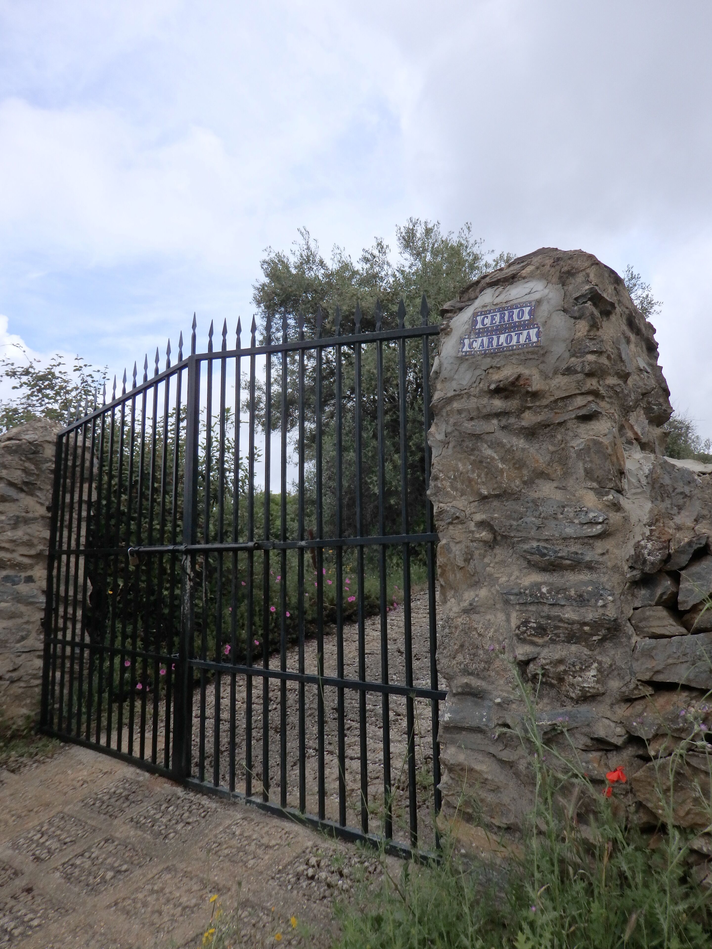 Um muro de pedra com um portão de metal e uma placa que diz 'CERRO CARLOTA'.