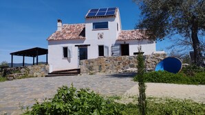 Un edificio blanco con techo de tejas, pared de piedra y un panel solar.