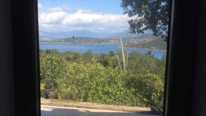 A view through a window of a tiled patio area with a body of water and distant hills in the background. - Coti Chiavari: House / Villa - Coti-chiavari (Coti-Chiavari)