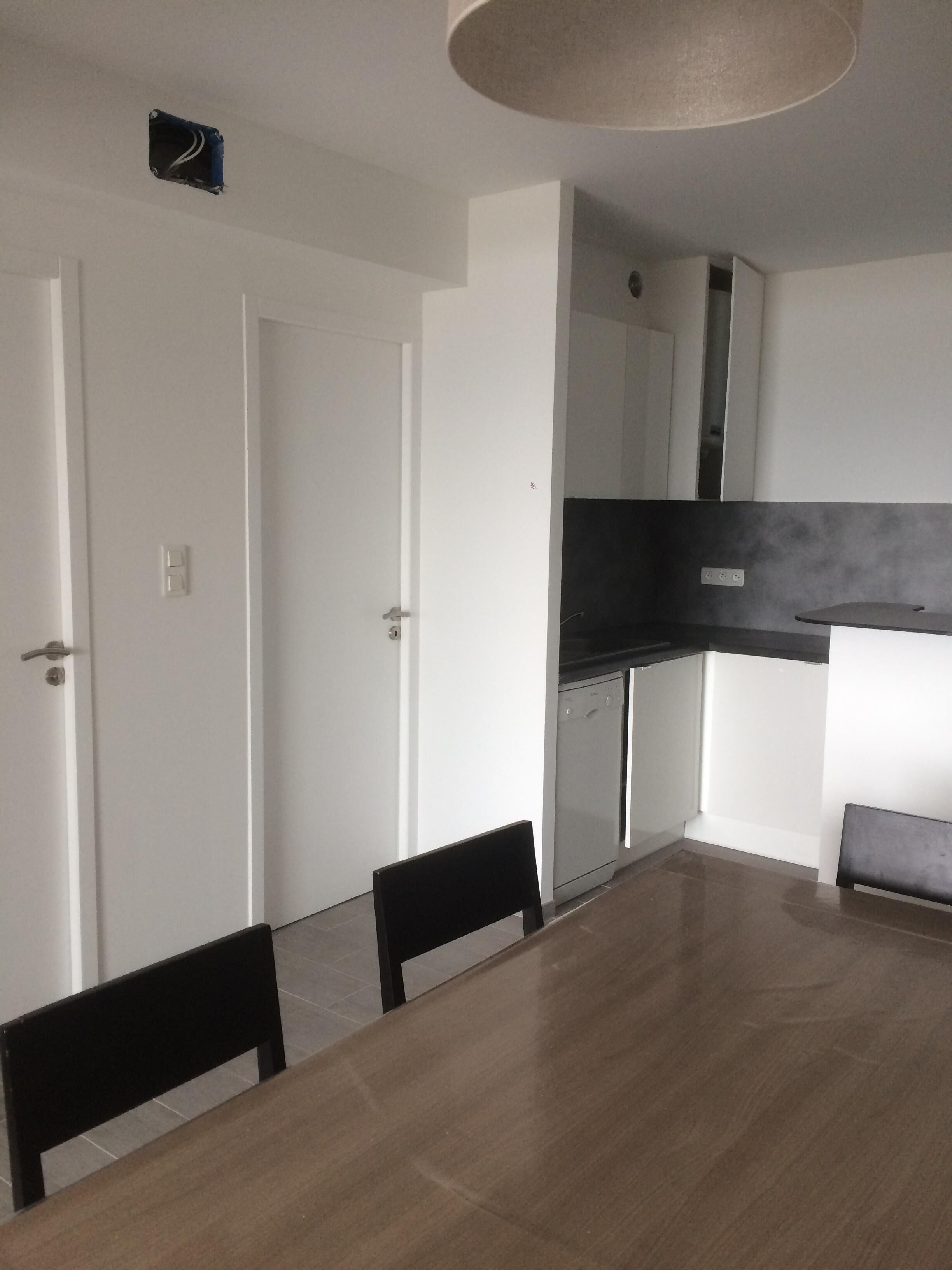 A modern kitchen with a black countertop and a built-in oven. There is a dining table with four chairs and a ceiling light fixture.