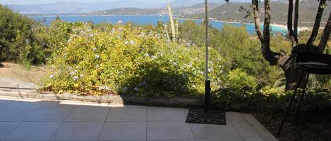 A patio with two lounge chairs, a striped umbrella, and a view of a lake and mountains.