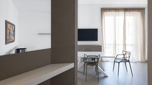 A modern living room with a flat-screen TV, a dining table with two chairs, and a large window with sheer curtains. - Design and Comfort in the Heart of Catania by Wonderful Italy (Catania)