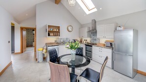 Een moderne keuken met een ronde glazen tafel, zwarte stoelen, een roestvrijstalen koelkast en een dakraam.