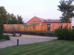 A rustic building with a stone wall and a wooden door, surrounded by a well-maintained lawn and trees. - Private lodge with countryside views and Hot tub (Ilminster)
