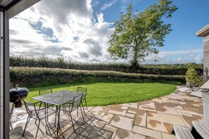 A patio with a table and chairs, a barbecue grill, and a well-maintained lawn with a hedge and tree. - Private lodge with countryside views and Hot tub (Ilminster)