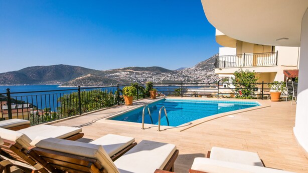 Ein Poolbereich mit Liegestühlen, einem Pool und Blick auf das Meer und die Berge.