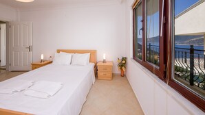Ein Hotelzimmer mit Bett, Nachttischen mit Lampen, einem Fenster mit Meerblick und einem Balkongeländer.