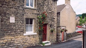 Un bâtiment en pierre avec une porte rouge, une fenêtre à cadre blanc et une enseigne sur le mur.