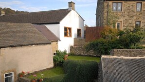 Une maison traditionnelle en pierre, avec une façade blanche, un toit en pente et un petit jardin agrémenté de plantes en pot.