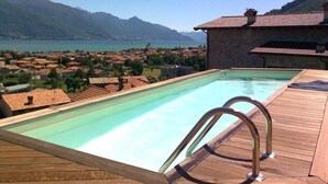 Una piscina con cubierta de madera y barandales de metal, con vista a un lago y montañas.