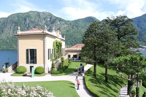 A building with a tiled roof, surrounded by well-maintained gardens and a lake. - House / Villa - DONGO House with character (Dongo)