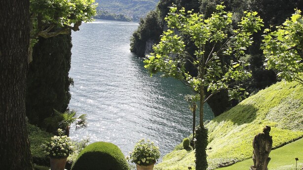 Una vista tranquila del lago con un sendero, plantas en macetas y una estatua.