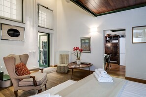 Une pièce spacieuse avec un grand lit, une chaise, une table ornée d’un vase de fleurs, et une vue sur la cuisine et la salle à manger, grâce à une porte ouverte.