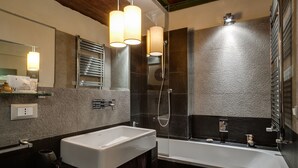 A modern bathroom with a large white bathtub, a glass-enclosed shower, and a mirror above the sink. - NAVONA ROMANTIC LOFT (Roma)