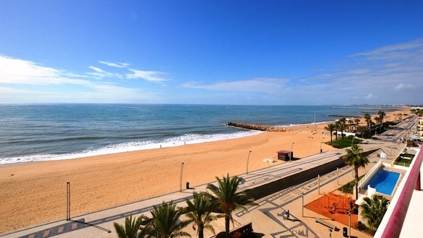 Blick auf einen Strand mit blauem Himmel, sandigem Ufer und einem Gebäude mit Schwimmbad.