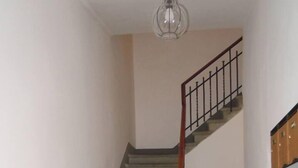En trappe med et trægelænder og metalspind, der fører op til en etage. Væggene er simple, og gulvet er fliset med terracotta og grå fliser.