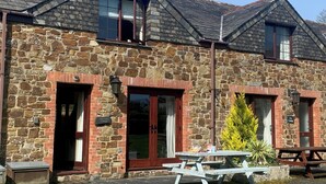A stone building with two visible doors and windows, a picnic table, and a small trash bin. - Cosy family cottage with dog-friendly garden, near Rock, Polzeath & Padstow (Wadebridge)