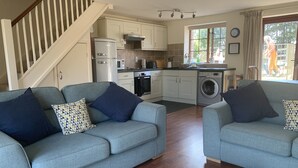 A modern kitchen with white cabinets, a microwave, stove, and a washing machine. There are two grey sofas with blue cushions. - Cosy family cottage with dog-friendly garden, near Rock, Polzeath & Padstow (Wadebridge)