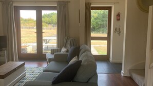 A living room with a sofa, a small table, and a TV. There are curtains on the windows, and a fire extinguisher is mounted on the wall. - Cosy family cottage with dog-friendly garden, near Rock, Polzeath & Padstow (Wadebridge)