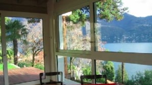 Une pièce avec une table et des chaises vertes, de grandes fenêtres donnant sur un lac et des montagnes.